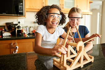 two young girls wearing safety goggles while playing with a miniature catapault