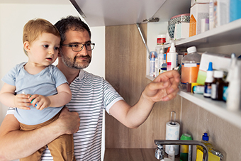 Dad holding toddler son while reaching into medicine cabinet